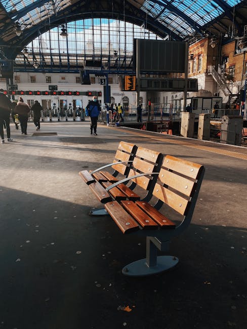 Outside Camden Town Station entry with a red-brick facade, large arched windows, and a blue sign indicating the station name. The underground roundel logo is visible above the entrance. In front, a diverse group of pedestrians, some carrying backpacks or shopping bags, are walking on the pavement near the entrance. The scene includes a wooden bench and a street scene with natural daylight. This setting relates to house removals and moving logistics by illustrating a common suburban or urban transit point near Leytonstone Station and Cann Hall, supporting the context of local relocations and furniture transport services provided by Man with Van Cann Hall, particularly during home relocation and packing and moving activities.